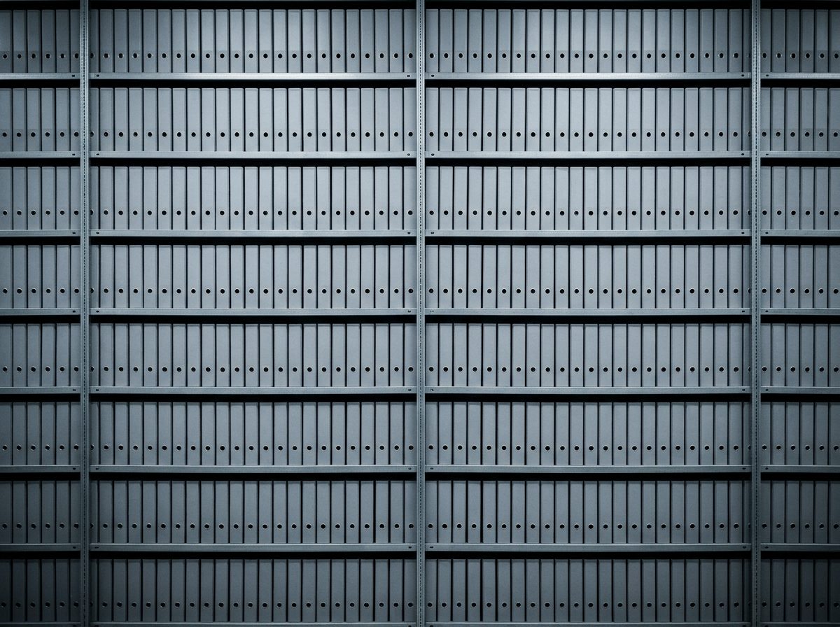 Wall of identical grey archive binders on steel shelving